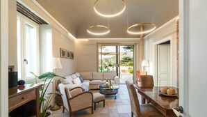 Un salon spacieux avec un grand canapé, une table à manger et une table basse. Il y a deux luminaires suspendus et une grande fenêtre qui laisse entrer la lumière naturelle.