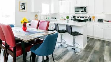 Una cucina moderna con mobili bianchi, un'isola centrale e un'area da pranzo con sedie rosse e blu.