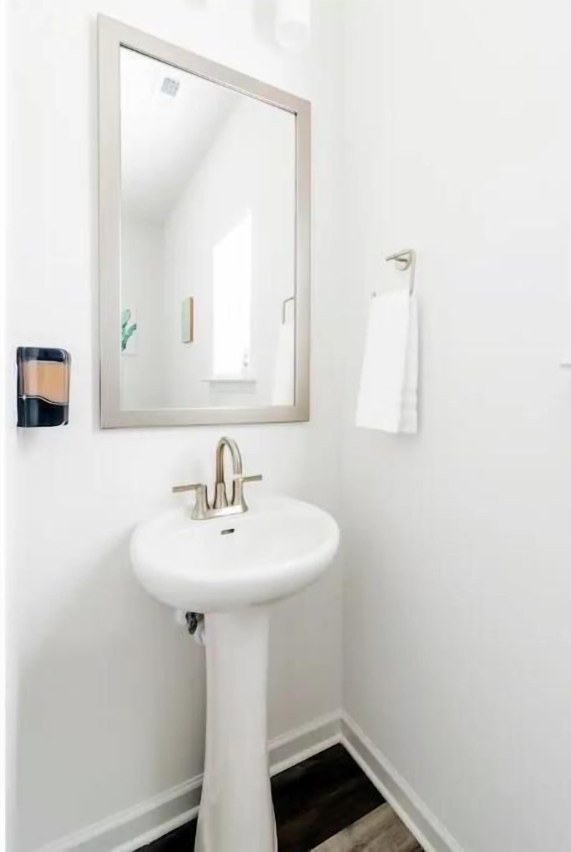 Un baño con un lavamanos blanco, un espejo y una toalla colgada en la pared.
