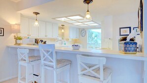 A modern kitchen with white cabinetry, a central island with bar stools, pendant lighting, and a large window providing natural light.
