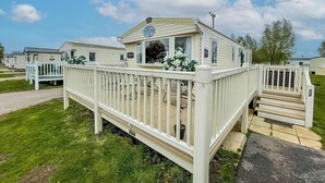 A mobile home with a porch and a small deck, surrounded by other similar homes. - Caravansleeps8-hottub-fireplace-garden-patio (Lincoln)