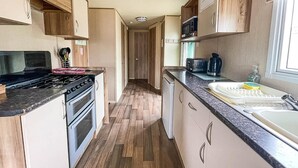 A narrow kitchen with wooden cabinets, a stove, and a microwave. - Caravansleeps8-hottub-fireplace-garden-patio (Lincoln)