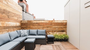 A wooden deck with a sectional sofa and a small table, surrounded by potted plants. - 50 Exchange Street Portland- 3B 
 (Portland)