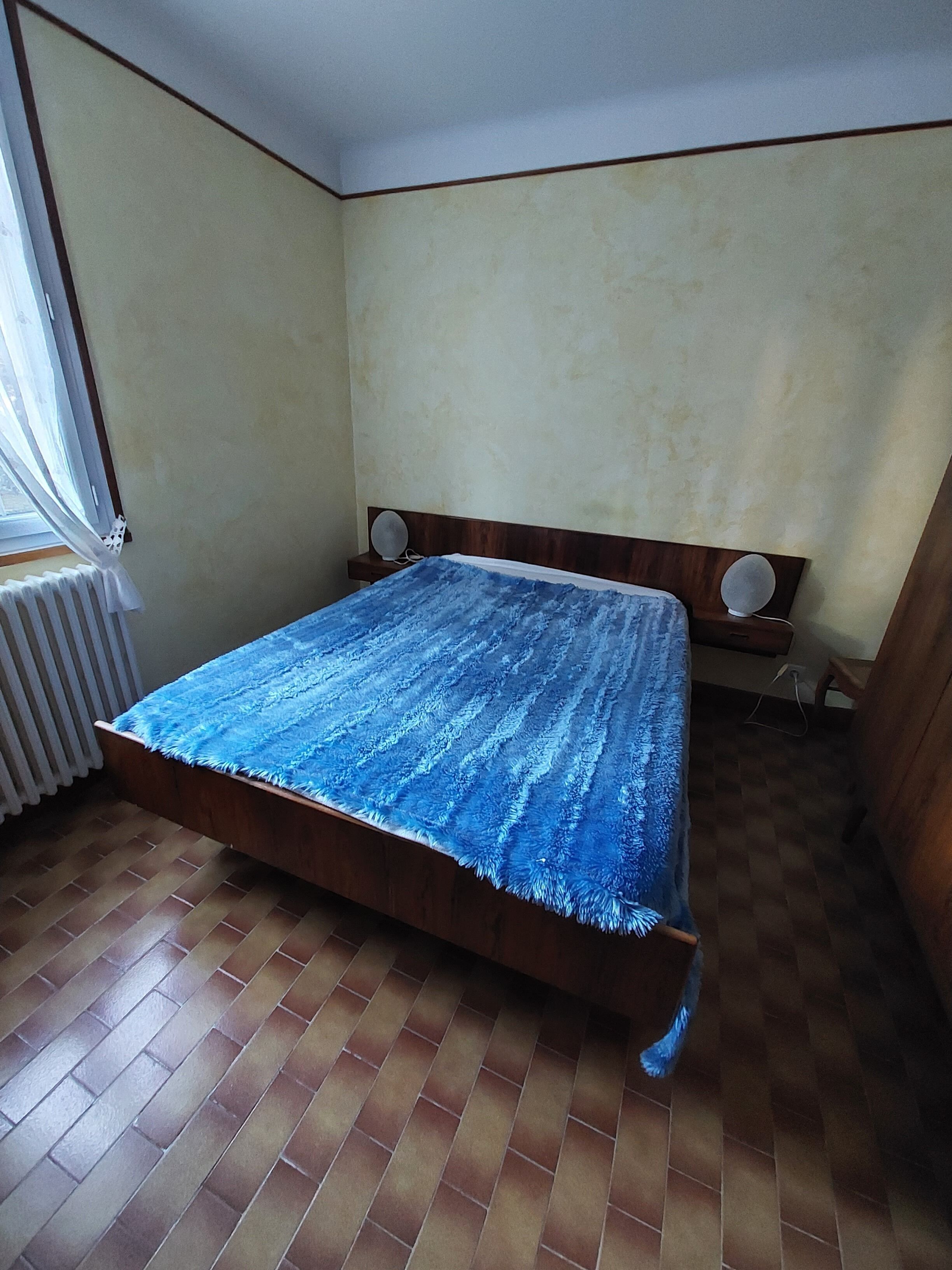 A bedroom with a wooden bed, a radiator, and a window with curtains.