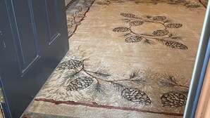 A wooden door with a metal handle, a patterned rug with pinecones and branches, and a wooden wall with a window. - White Bluff Cabin overlooking Lake Malone  (Lewisburg)