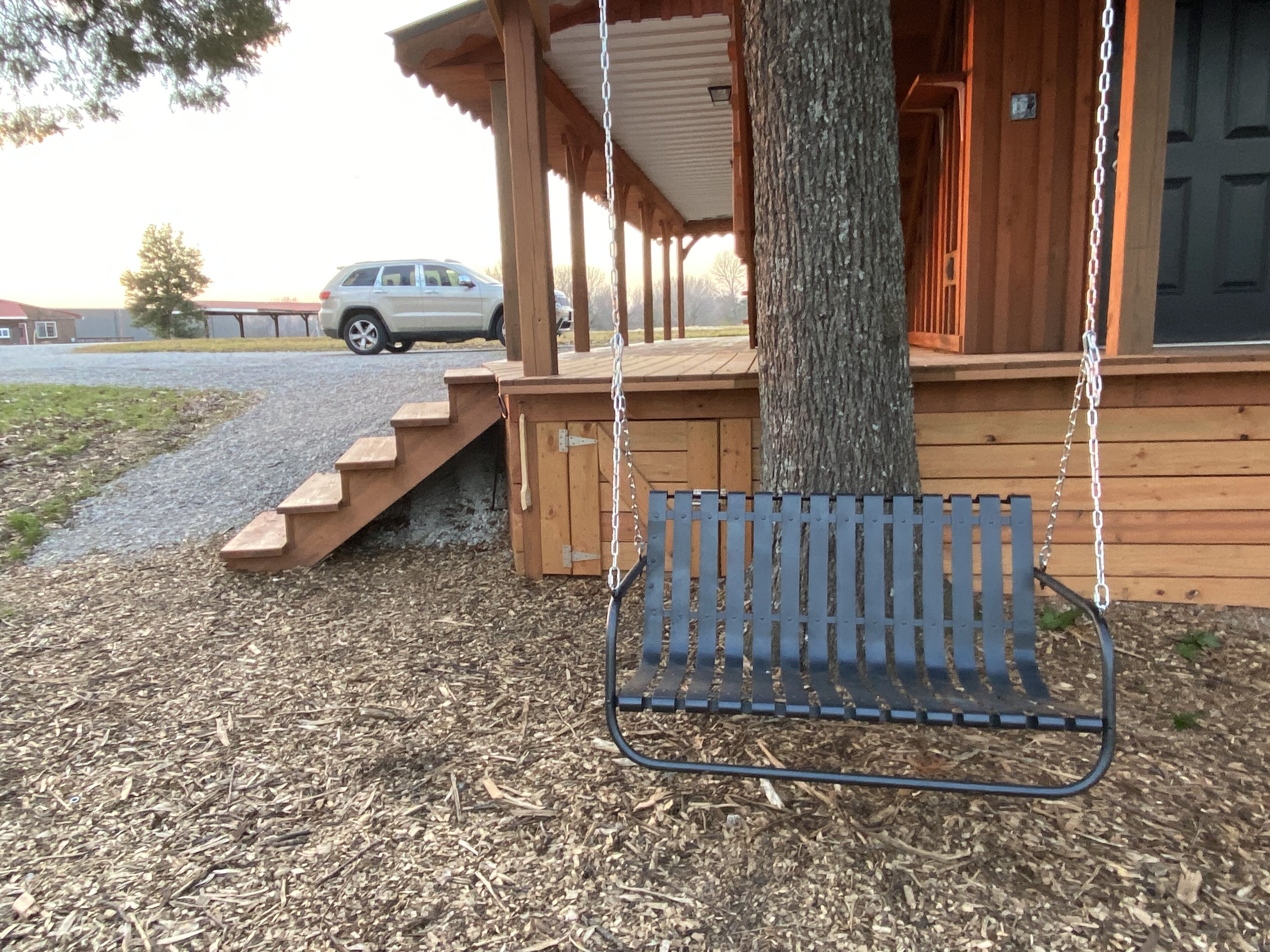 Una cabana de fusta amb un seient d'àmples, una escala de fusta i un arbre.