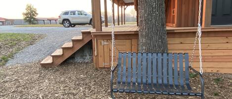 Una cabana de fusta amb un seient d'àmples, una escala de fusta i un arbre.