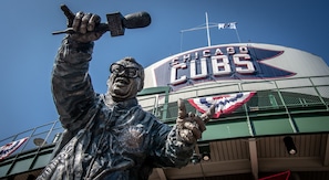 Eine Statue eines Mannes mit Mikrofon, einem Cubs-Logo und einer Flagge an einem Gebäude.