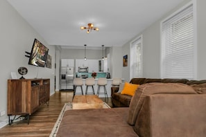 A modern living room with a brown sofa, a wooden cabinet, and a kitchen in the background. - Cozy Train Vibes + Rare Parking x3 (Chicago)
