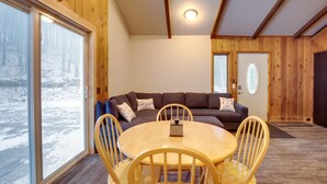 Una habitación acogedora con detalles de madera, una mesa redonda con sillas, un sofá con cojines y una puerta con un panel de vidrio esmerilado.