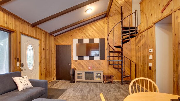 Una habitación acogedora con paredes de madera, un sofá, una mesa y una escalera de caracol.