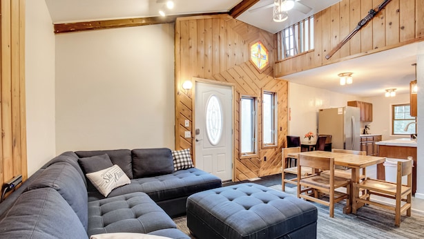 Uma sala de estar moderna com sofá modular, um apoio para os pés, detalhes em madeira e uma área de jantar com mesa e cadeiras.