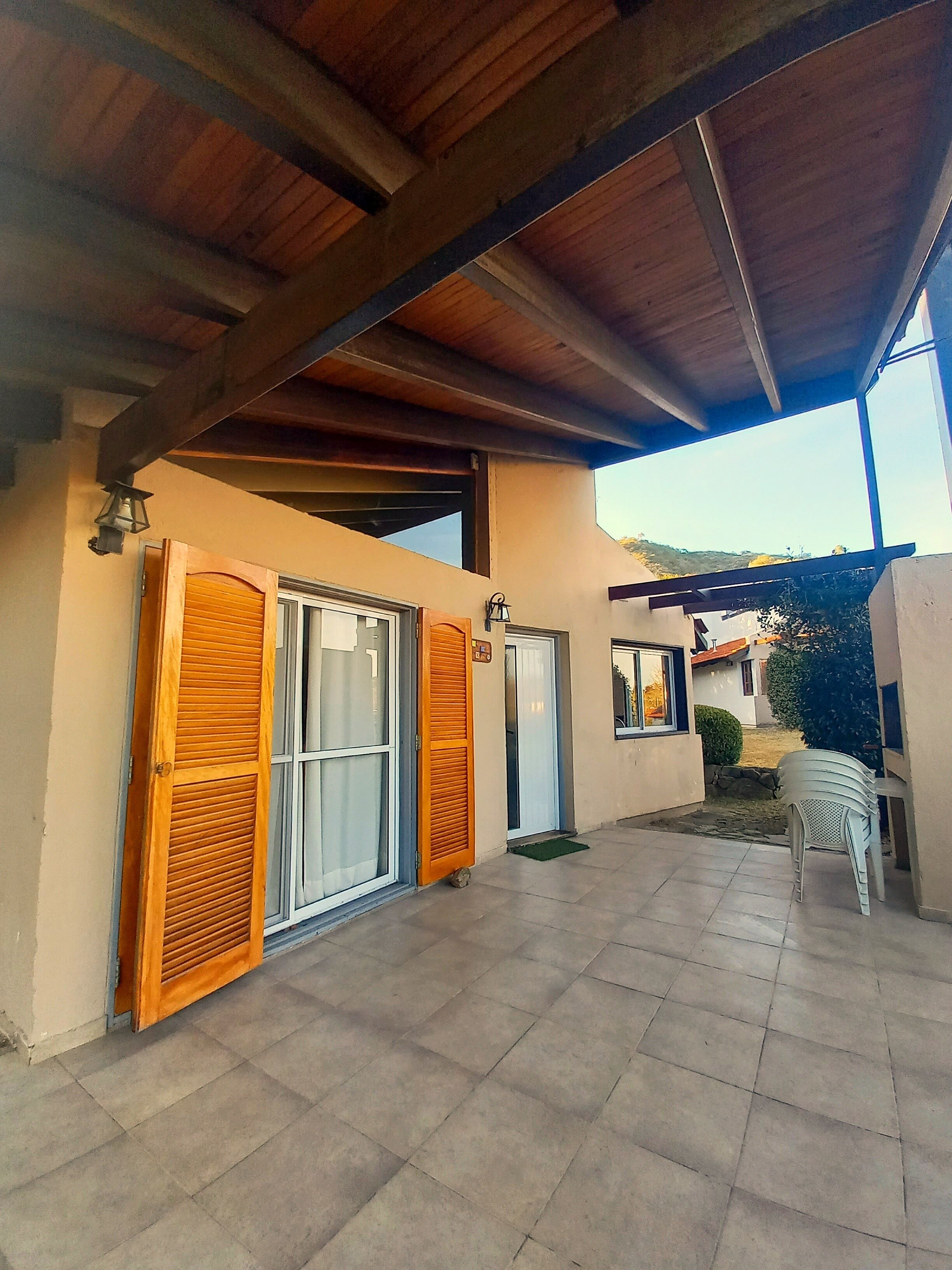 A covered outdoor area with a tiled floor, wooden shutters on a door, and a small table with chairs.