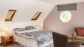 A bedroom with a bed, two bedside tables, a chair, a window, and a skylight.