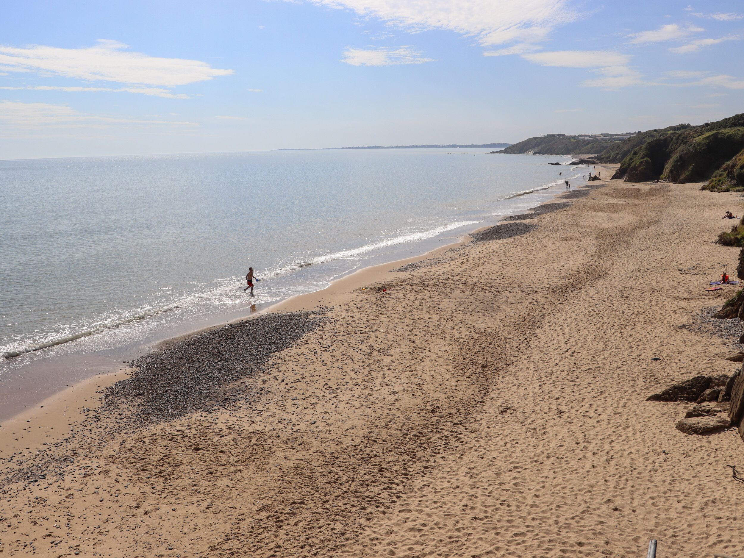 A beach with a wide sandy shore, a clear sky, and a calm sea.