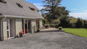 A house with a gravel driveway, a patio with outdoor furniture, and a large tree in the background.