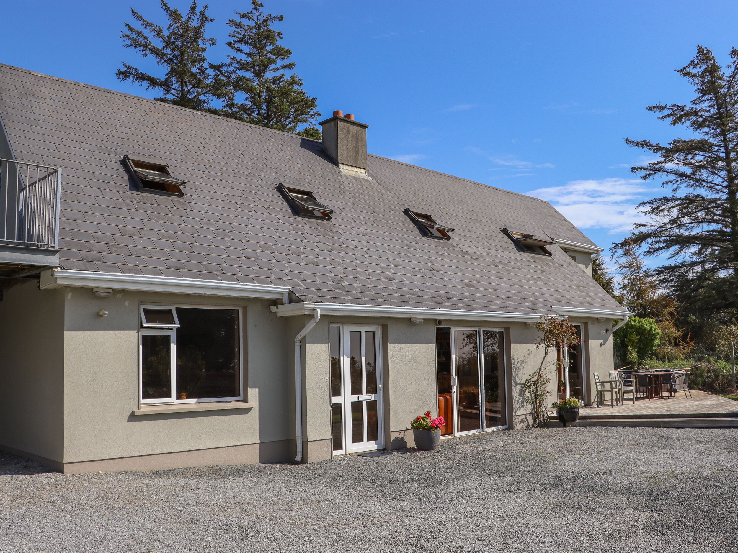 Une maison à deux étages avec un toit gris, de nombreuses fenêtres et une allée gravillonnée.