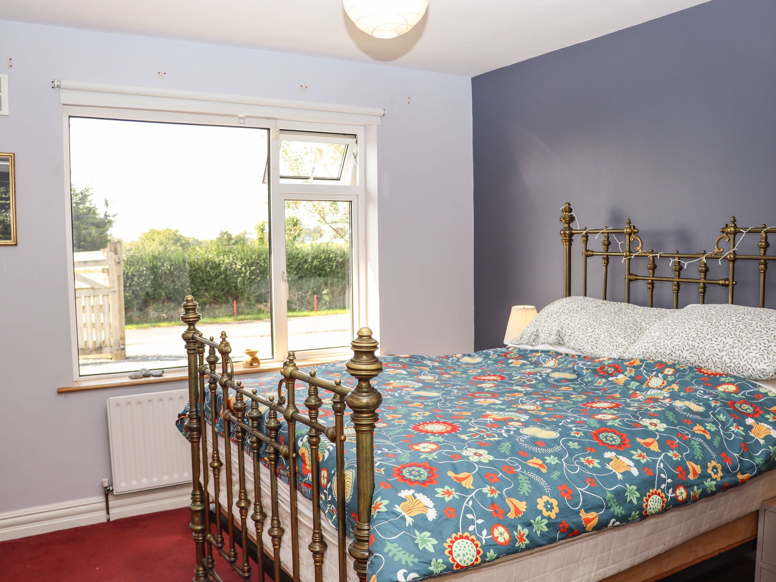 A bedroom with a large window, a bed with a floral bedspread, and a radiator.