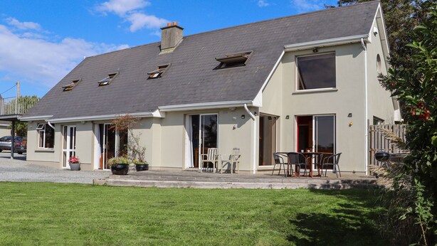 A two-story house with a sloped roof, a front porch with chairs, and a small garden area.