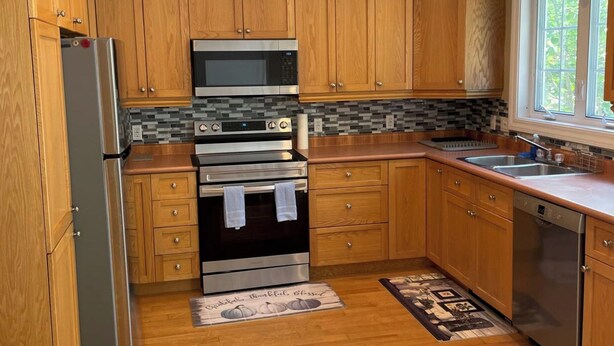 A modern kitchen with wooden cabinets, stainless steel appliances, a tiled backsplash, and a window providing natural light. - Lovely condo right beside Acadia (Bar Harbor)