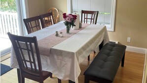A dining area with a table set for four, wooden chairs, a bench, and a vase with flowers. - Lovely condo right beside Acadia (Bar Harbor)
