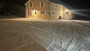 A two-story wooden house with a sloped roof, an American flag, and a well-lit front porch. - The Superior Lodge - Located On Trail - Pictured Rocks Lakeshore, Munising MI (Munising)