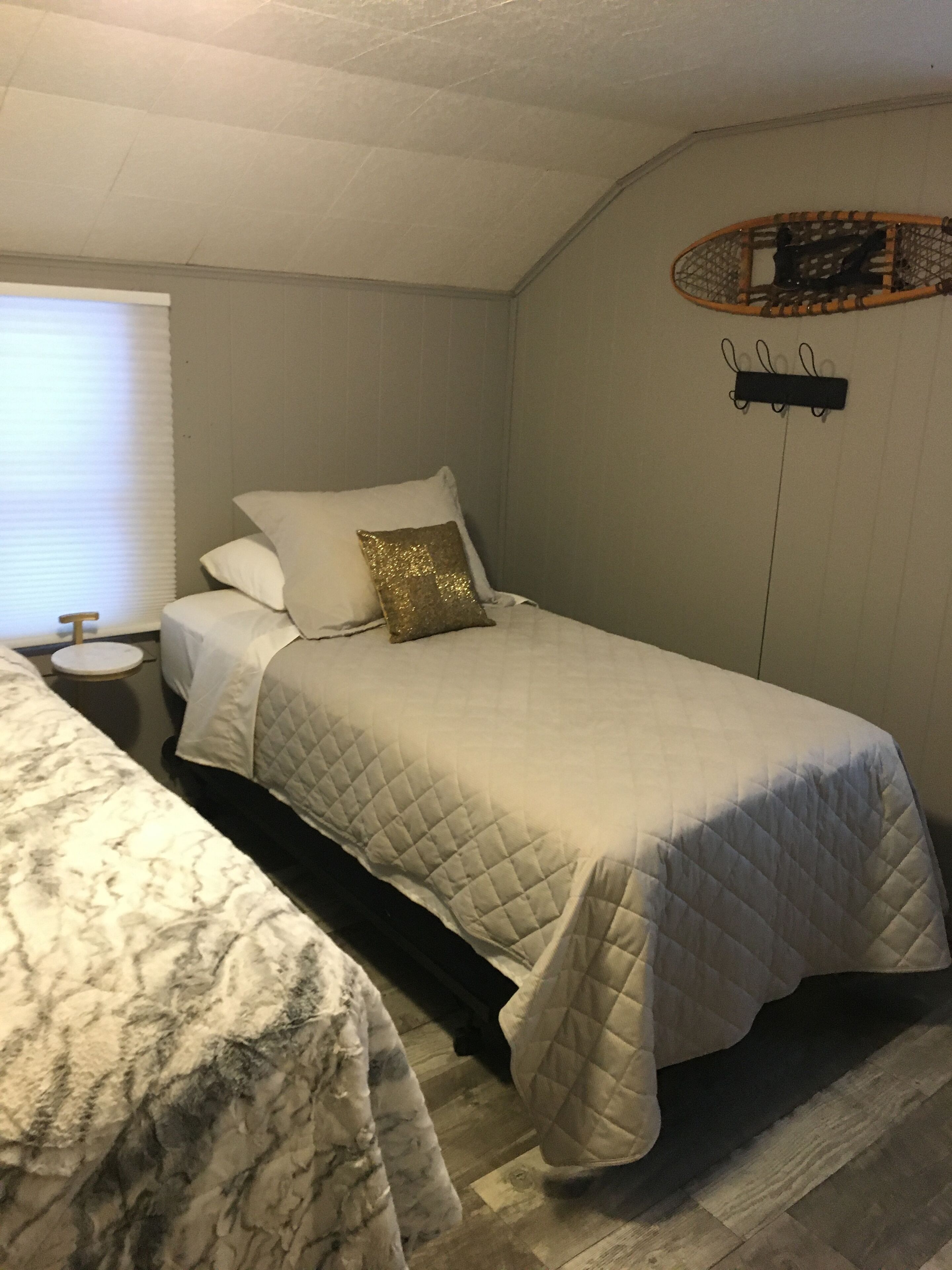 A bedroom with two beds, a small bedside table, a wall-mounted shelf, and a window with blinds.