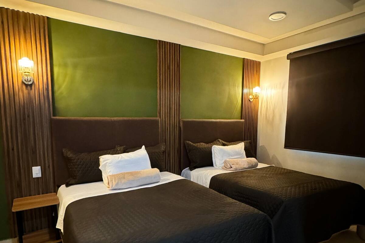 A hotel room with two beds, a wooden bench, and a large window.