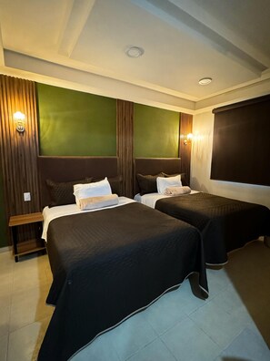 Quarto de hotel com duas camas, um banco de madeira e uma janela grande.