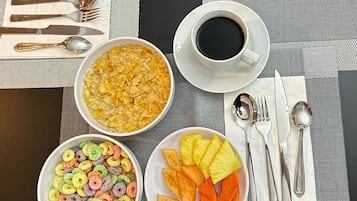 A breakfast setting with cereal, fruit, and coffee on a table.