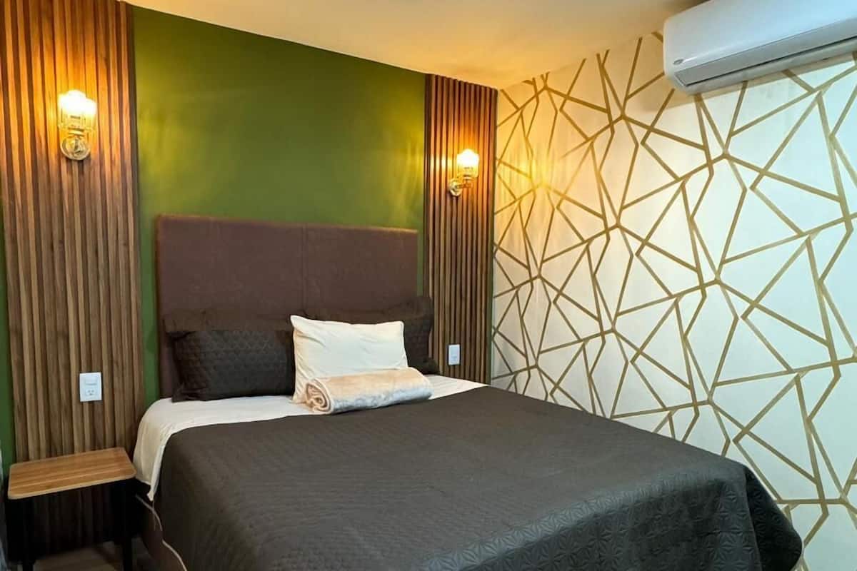 A neatly made bed with a dark cover, a bedside table, and two wall-mounted lamps.