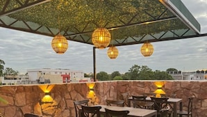 An outdoor dining area with tables and chairs, a stone wall, and hanging lanterns. - Royal Madero Inn Express (Tampico)