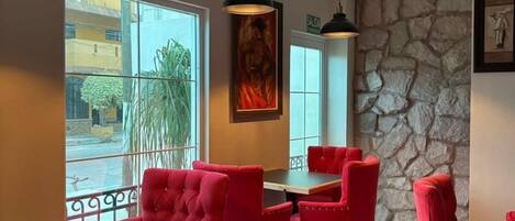 Un comedor con sillas tapizadas rojas, una mesa, iluminación colgante y una pared de piedra.