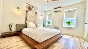 Ein modernes Schlafzimmer mit einem großen Bett, einer Wand-Klimaanlage und zwei Fenstern mit Pflanzen.