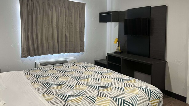 Une chambre d’hôtel équipée d’un lit, d’un téléviseur à écran plat fixé au mur, d’un bureau avec une lampe et d’une fenêtre avec des rideaux.