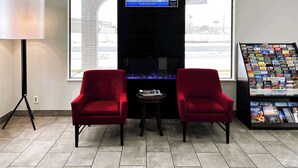 A lobby with two red chairs, a TV screen, a fireplace, and a travel information kiosk. - Studio 6 Ogden, Ut – 21St Street (Ogden)