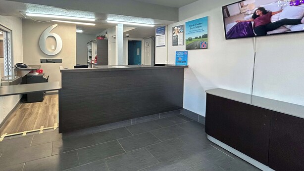 Un espace d’accueil avec un comptoir, un téléviseur fixé au mur et une porte bleue en arrière-plan.