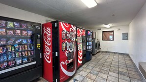 Des distributeurs automatiques de collations et de boissons, un sol carrelé et un mur sobre avec une fenêtre.