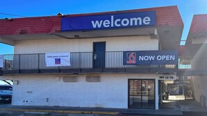 Un bâtiment avec une enseigne indiquant « Bienvenue », une autre indiquant « Ouvert maintenant » et une troisième indiquant « Motel de 6 chambres + studio ».