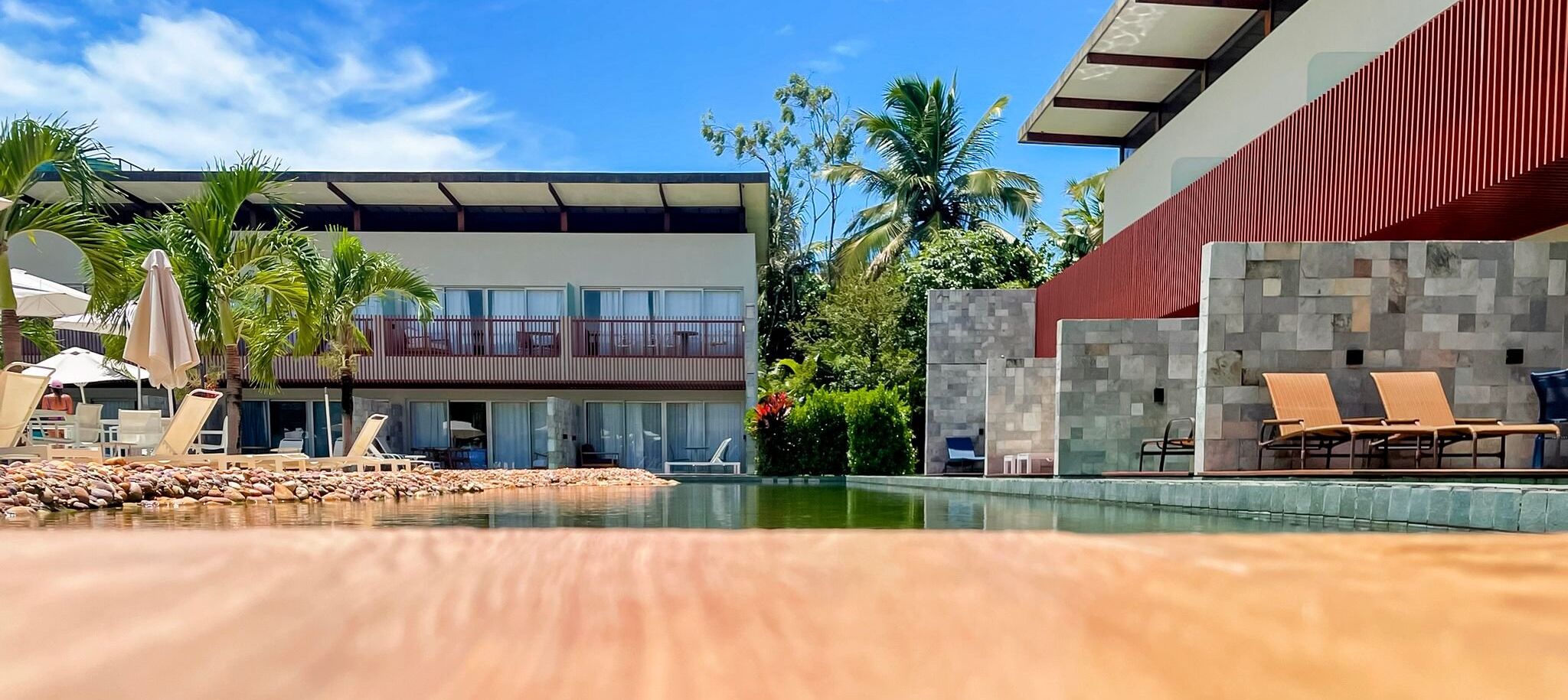 A modern hotel with a pool, lounge chairs, and palm trees.