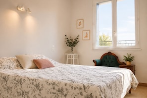 A bedroom with a bed, a window, a chair, and a small table with a plant.