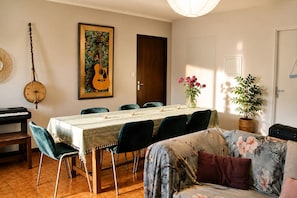 A dining area with a table, chairs, a piano, a guitar, and a painting.