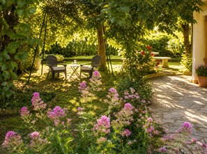 A garden patio with a table and chairs, surrounded by lush greenery and flowering plants. - House LA VILLANELLE: swimming pool, pétanque, quiet in the beautiful town of Uzès (Uzès)