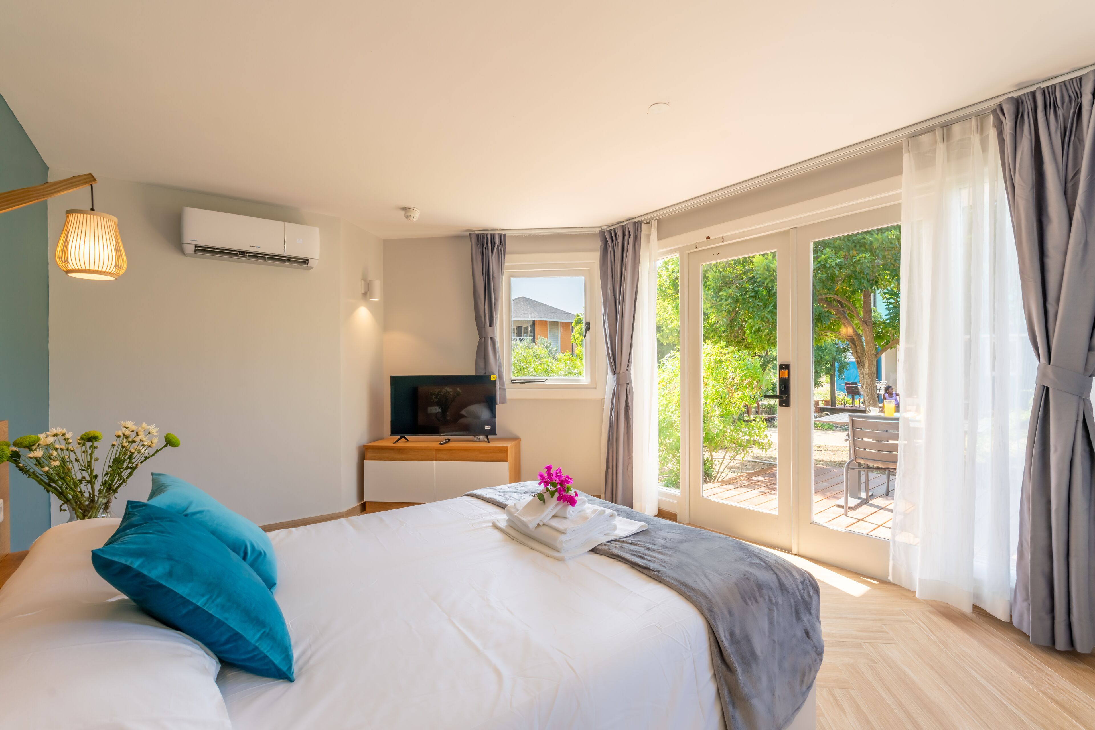 A hotel room with a bed, a desk with a TV, and a view of the outdoors.