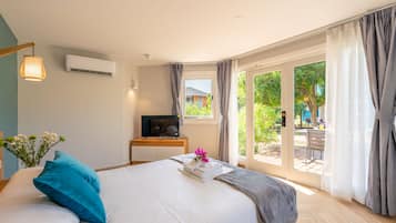 A hotel room with a bed, a desk with a TV, and a view of the outdoors.