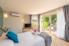 A hotel room with a bed, a desk with a TV, and a view of the outdoors.