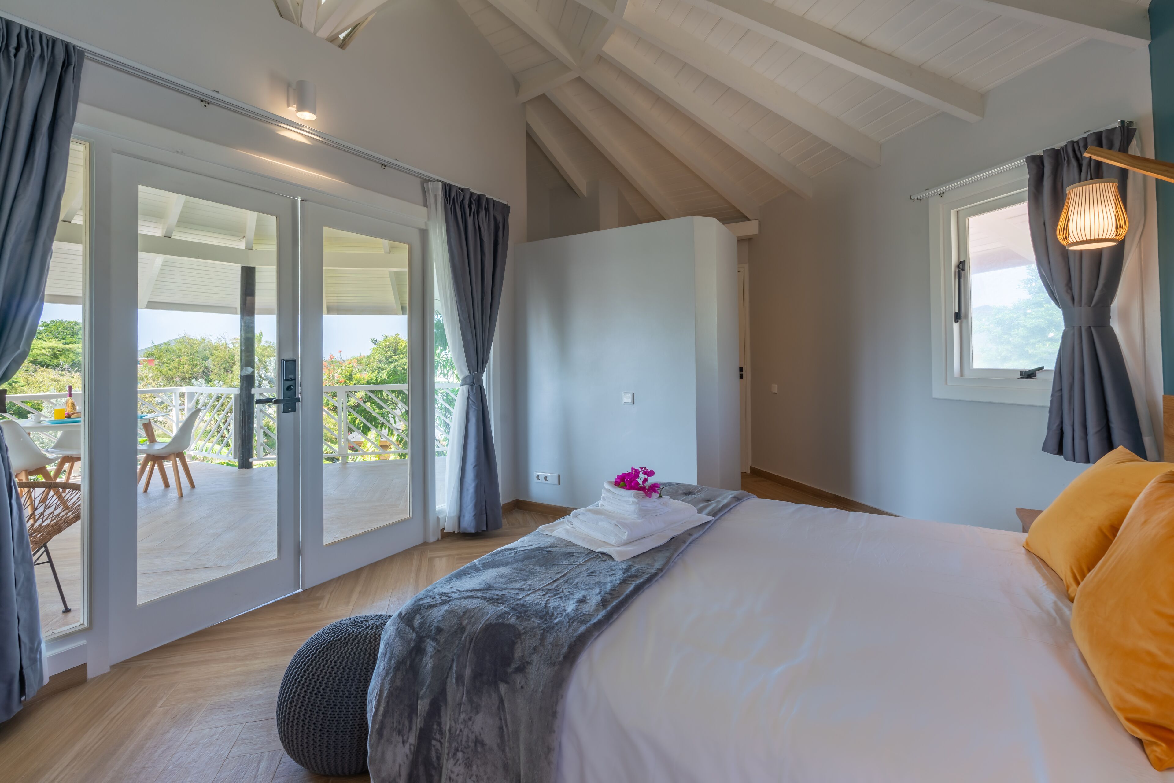 A bedroom with a large bed, a view of the outdoors, and a sliding glass door leading to a balcony.