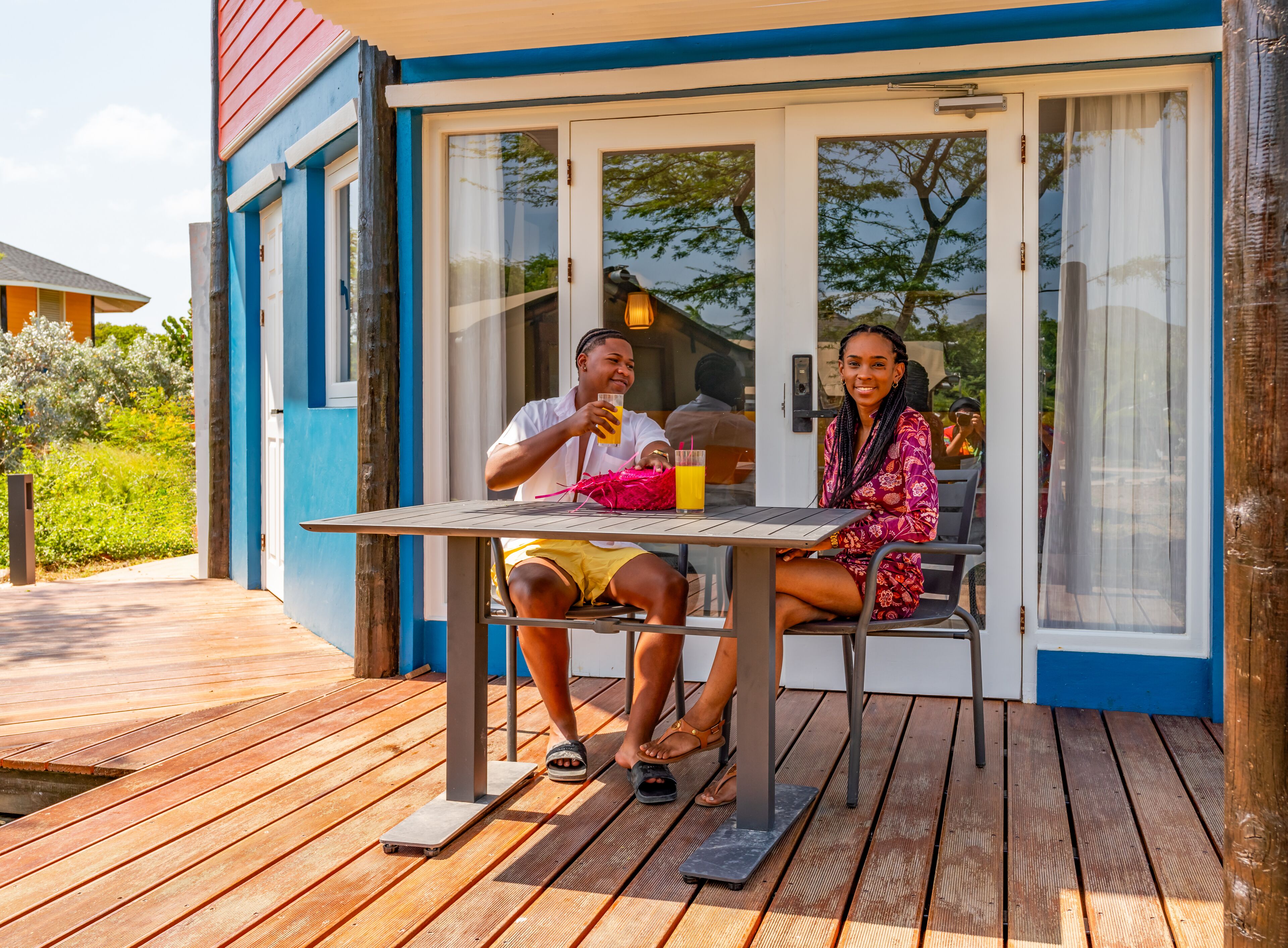 Ein Paar sitzt an einem Tisch im Freien, mit einer Holzterrasse, einer Glastür und Blick auf Grünflächen.