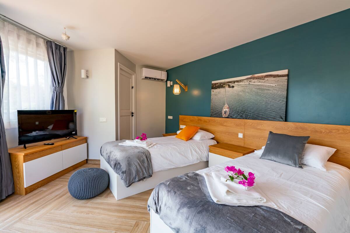 Una habitación de hotel moderna con dos camas, un televisor, un escritorio de madera y un cuadro en la pared.