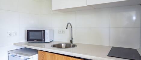 Una cocina con armarios blancos, un lavamanos de acero inoxidable, un microondas y un lavavajillas.